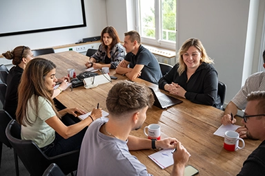 Gruppe Personen sitzt um einen Konferenztisch und bespricht etwas.