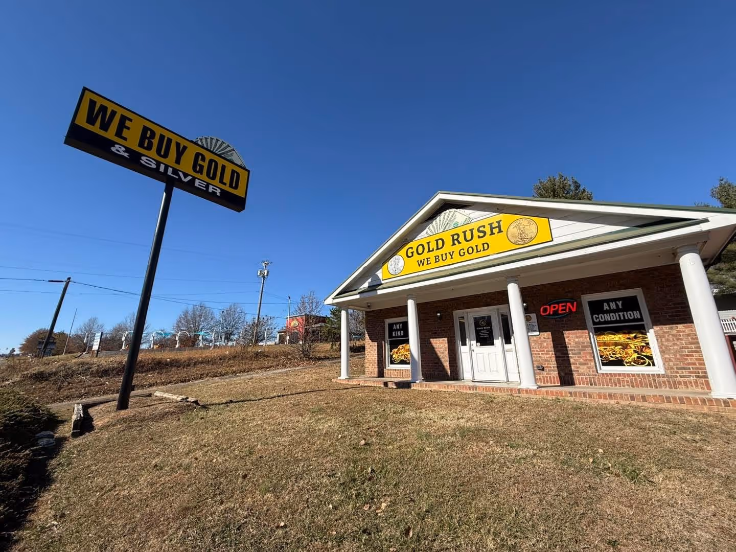 Gold Rush store building with yellow signs saying 'WE BUY GOLD & SILVER' and 'GOLD RUSH WE BUY GOLD' under a clear blue sky.