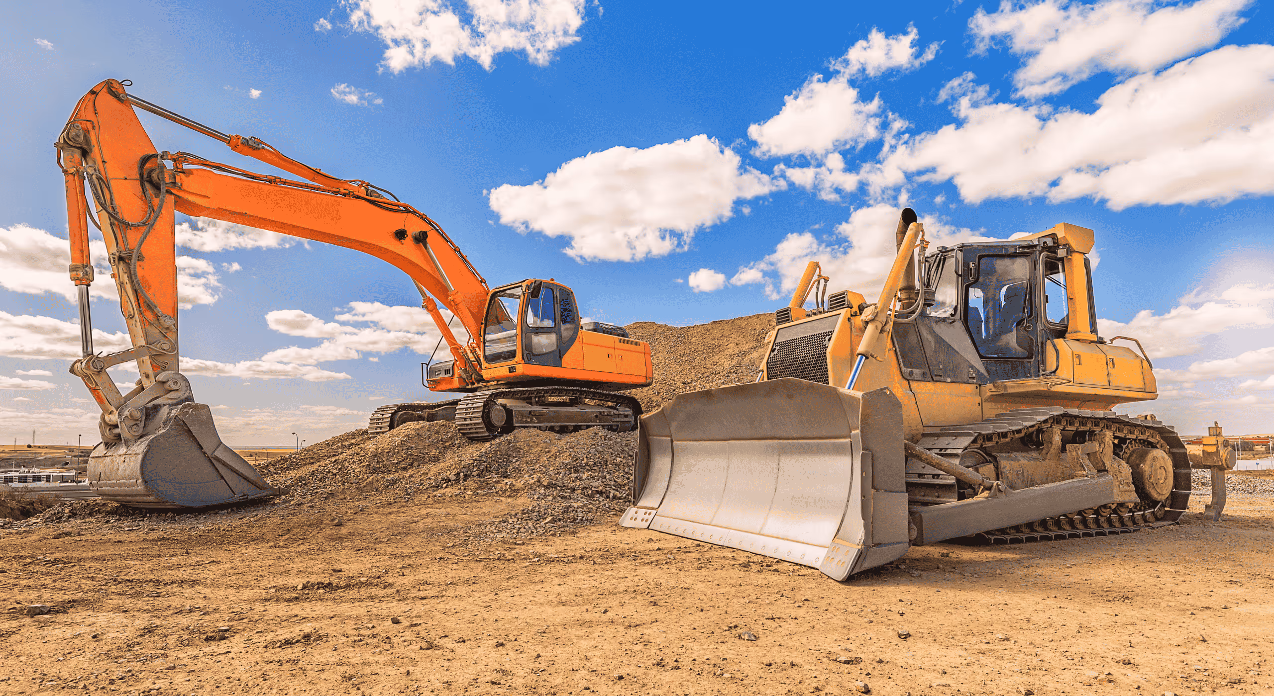 Orange excavator and yellow bulldozer on a dirt construction site under a partly cloudy blue sky.