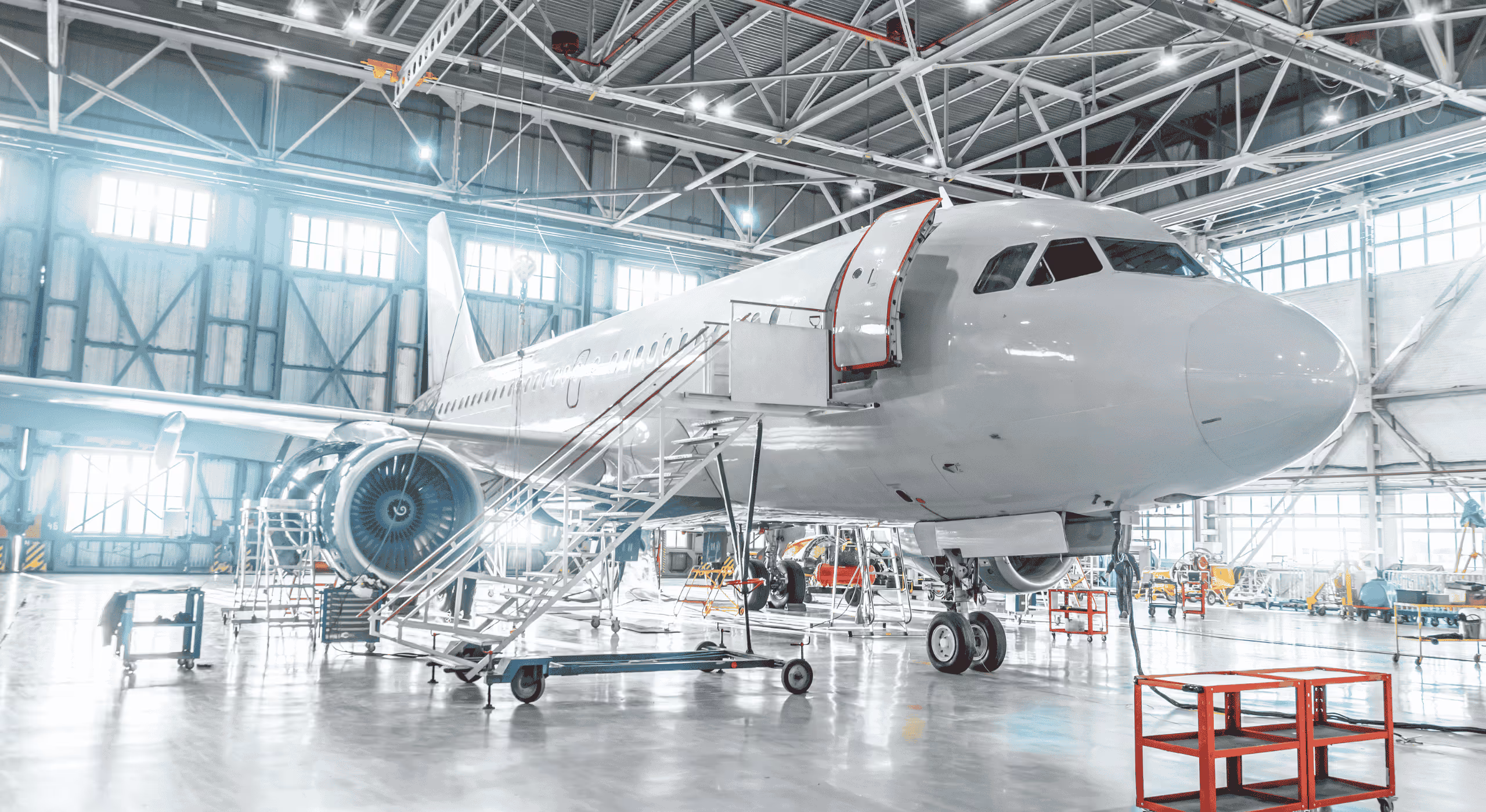 Large white airplane inside a spacious, well-lit aircraft hangar with maintenance equipment around.
