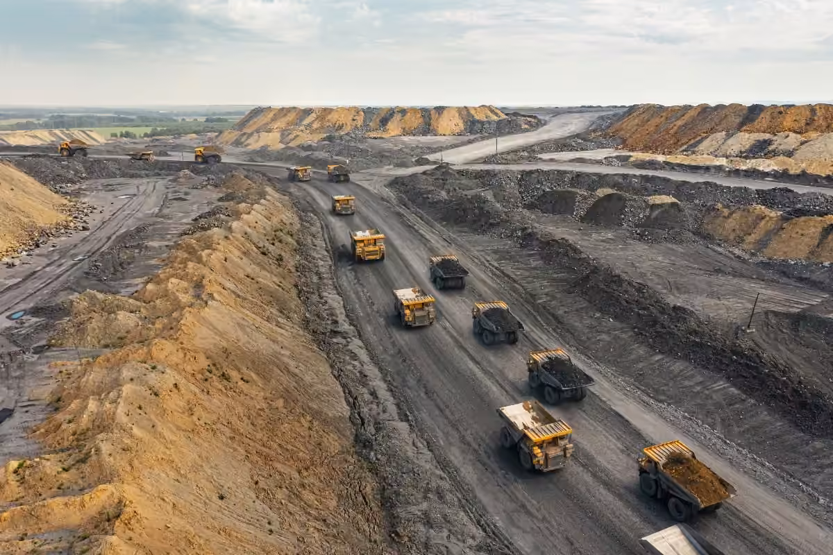 Aerial view of an open-pit mine with multiple large dump trucks carrying earth and minerals along dirt roads.