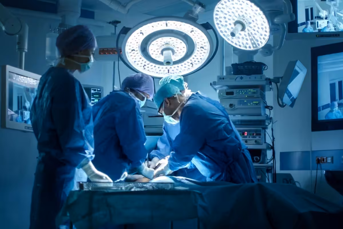 Surgical team in blue scrubs and masks performing an operation under bright operating room lights.