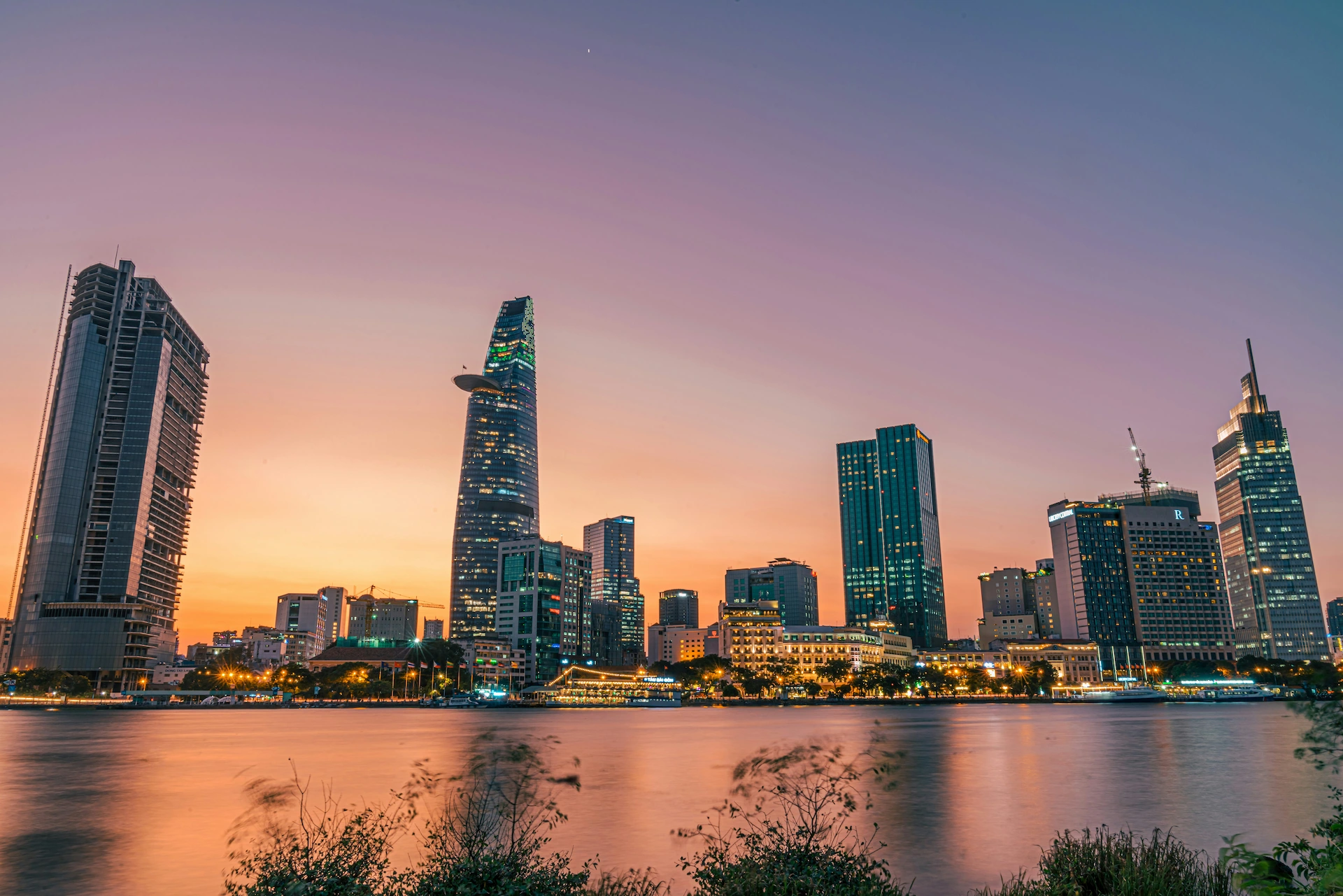 Sunset view of Ho Chi Minh City's skyline with modern skyscrapers and river reflections, highlighting the city's vibrant urban landscape.