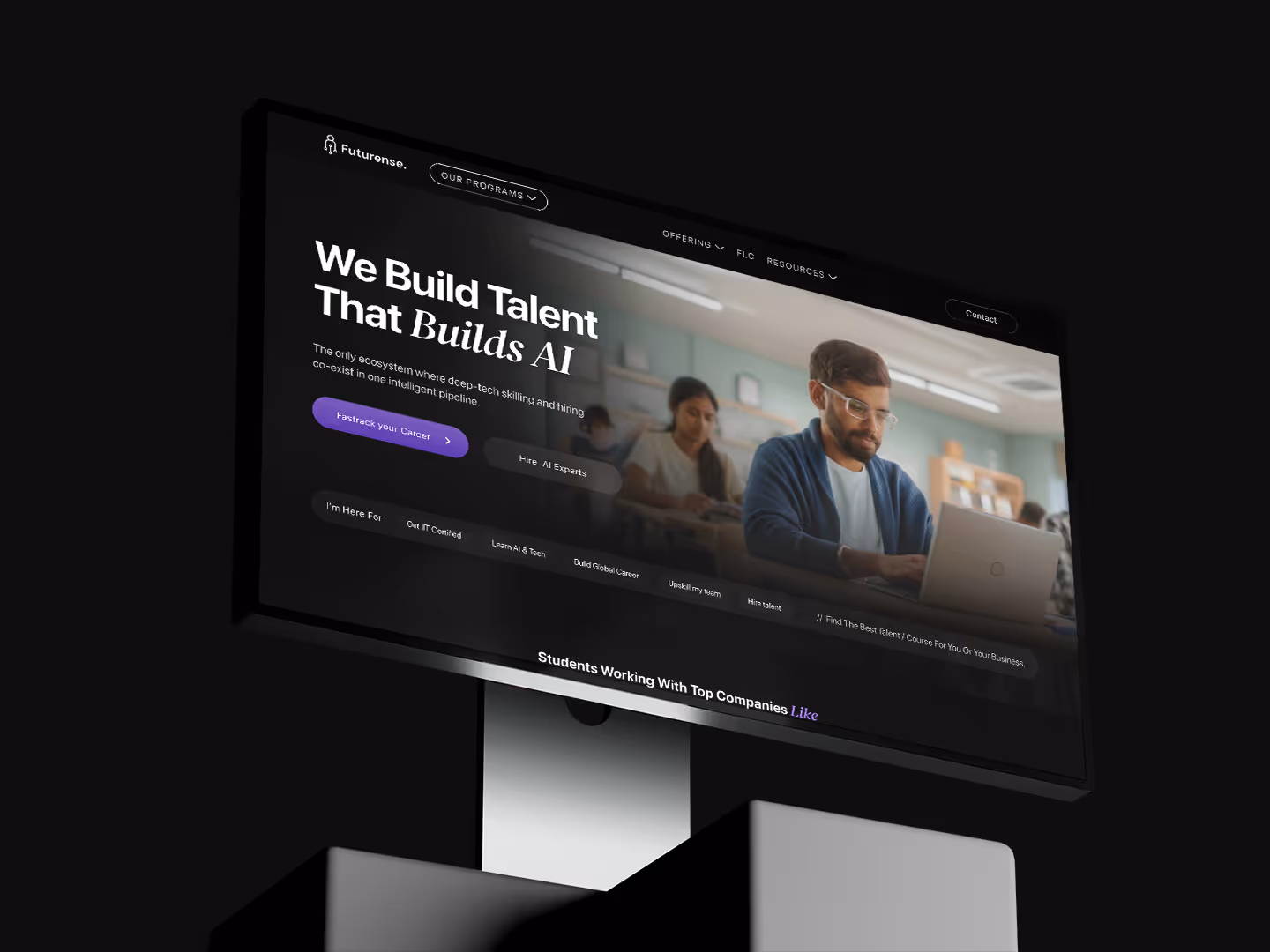 Computer monitor displaying Futurense website homepage featuring a man working on a laptop and text about building AI talent.