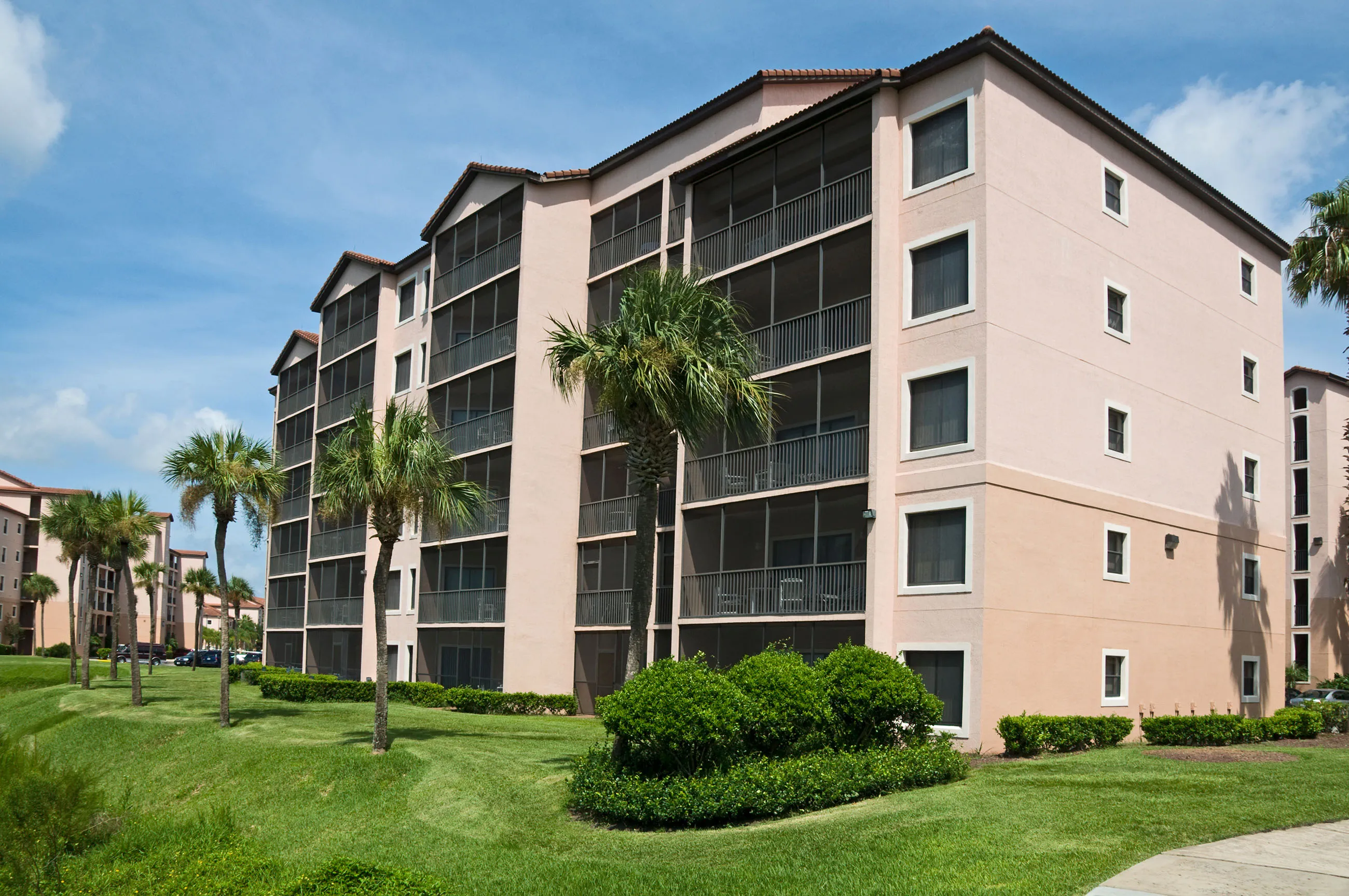 A 5 story hotel with lush grass and palm trees on the exterior 
