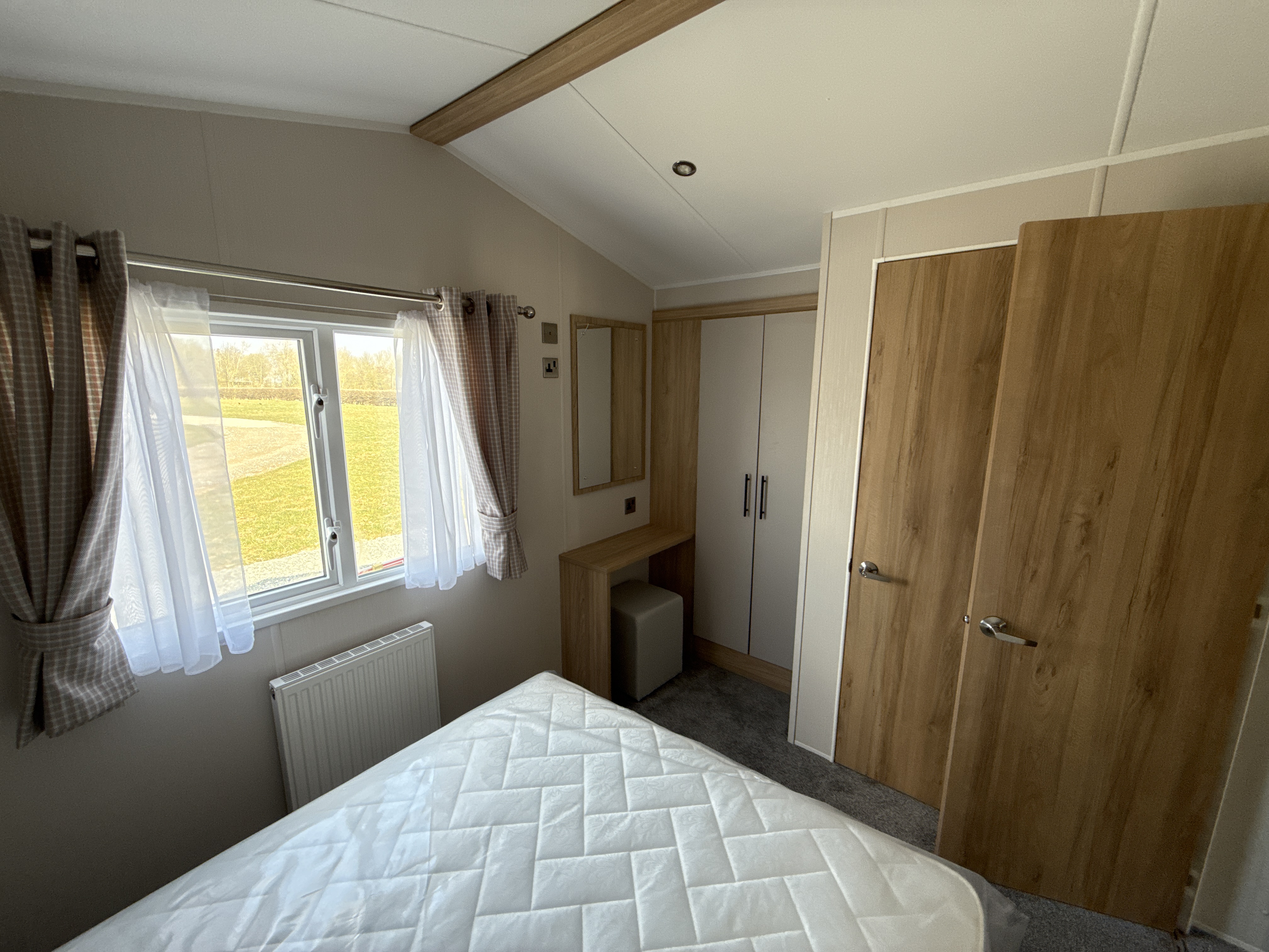 Cozy bedroom with white bedding, wooden wardrobe, and window overlooking grass
