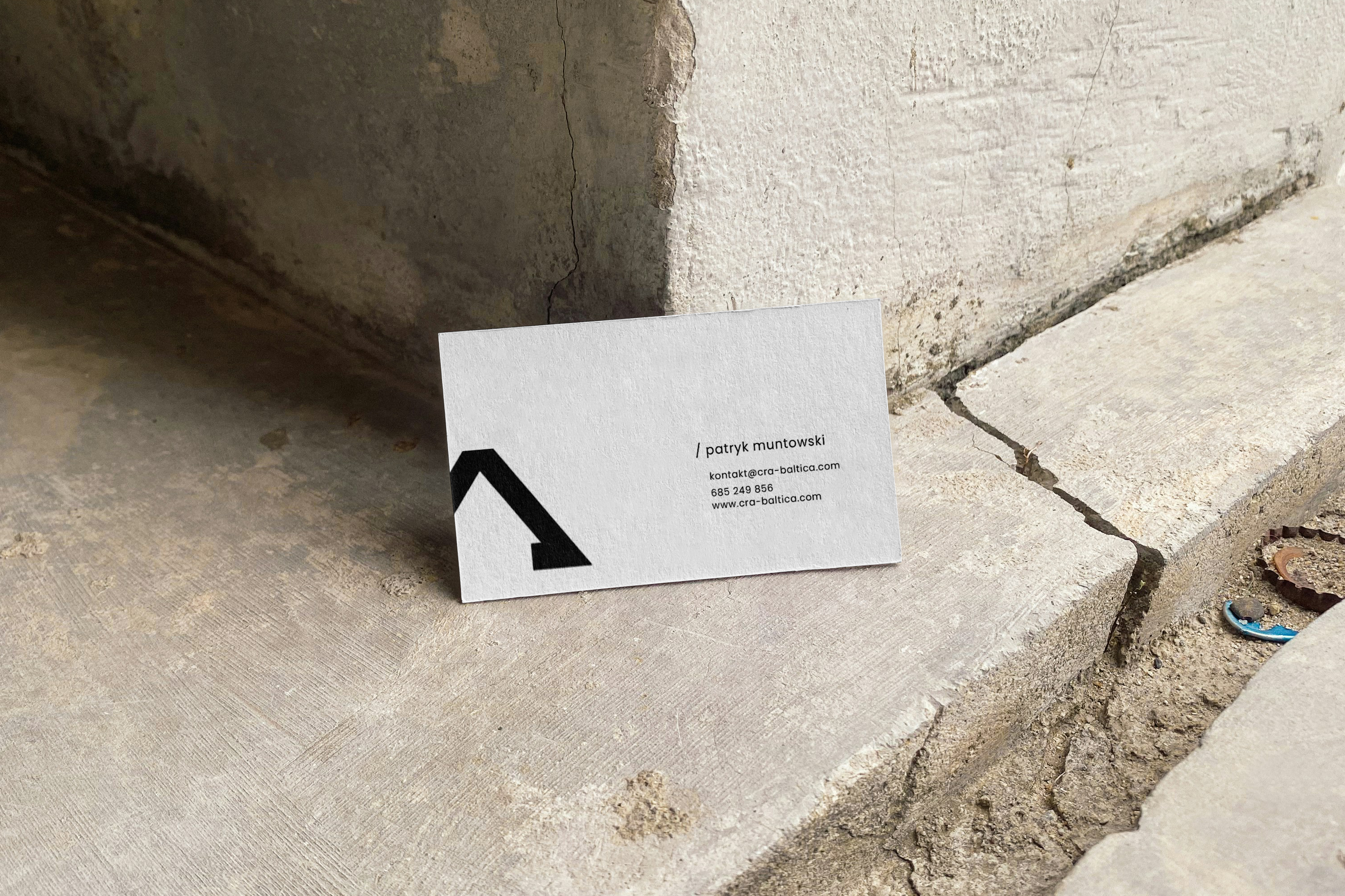 Visittkort design for CRA Baltica på sprukket betongoverflate. Minimalistisk design med svart geometrisk logo og kontaktinformasjon.