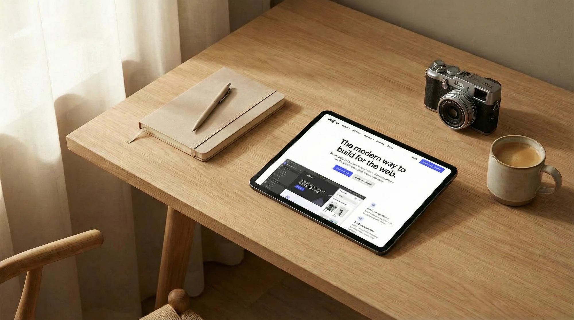 Oversiktsbilde av nettbrett på trebord som viser Webflow-nettside, ved siden av notatbok og et vintage kamera.