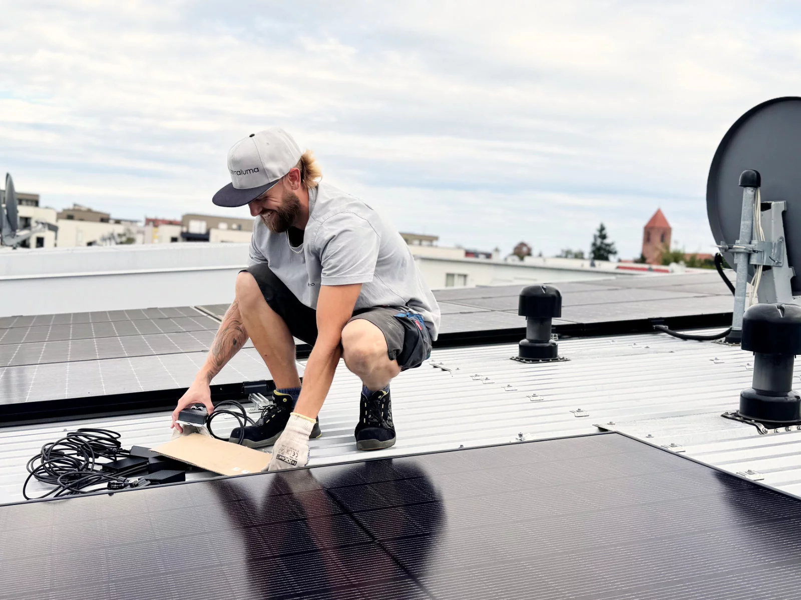Techniker von terraluma installiert Solarmodule auf Metalldach neben Satellitenschüssel