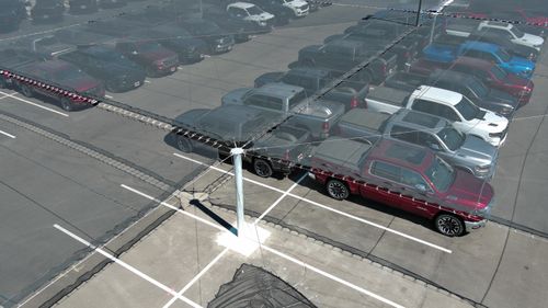 Cars parked in parking lot under hail netting, aerial side view