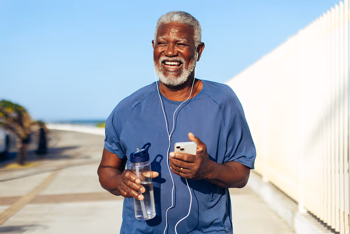 happy senior african american man exercising outside with headphones and water bottle