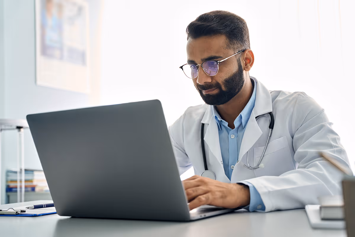 a handsome indian doctor working on a laptop in his office