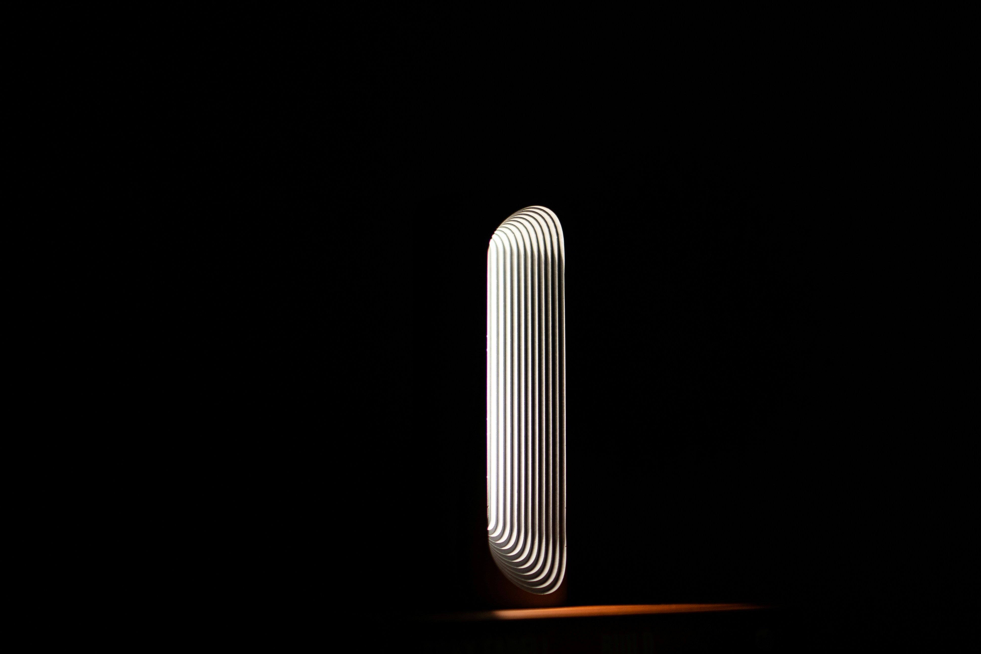 A glowing oval light form standing upright in complete darkness, its concentric ridges radiating outward, the stillness of the gap before action