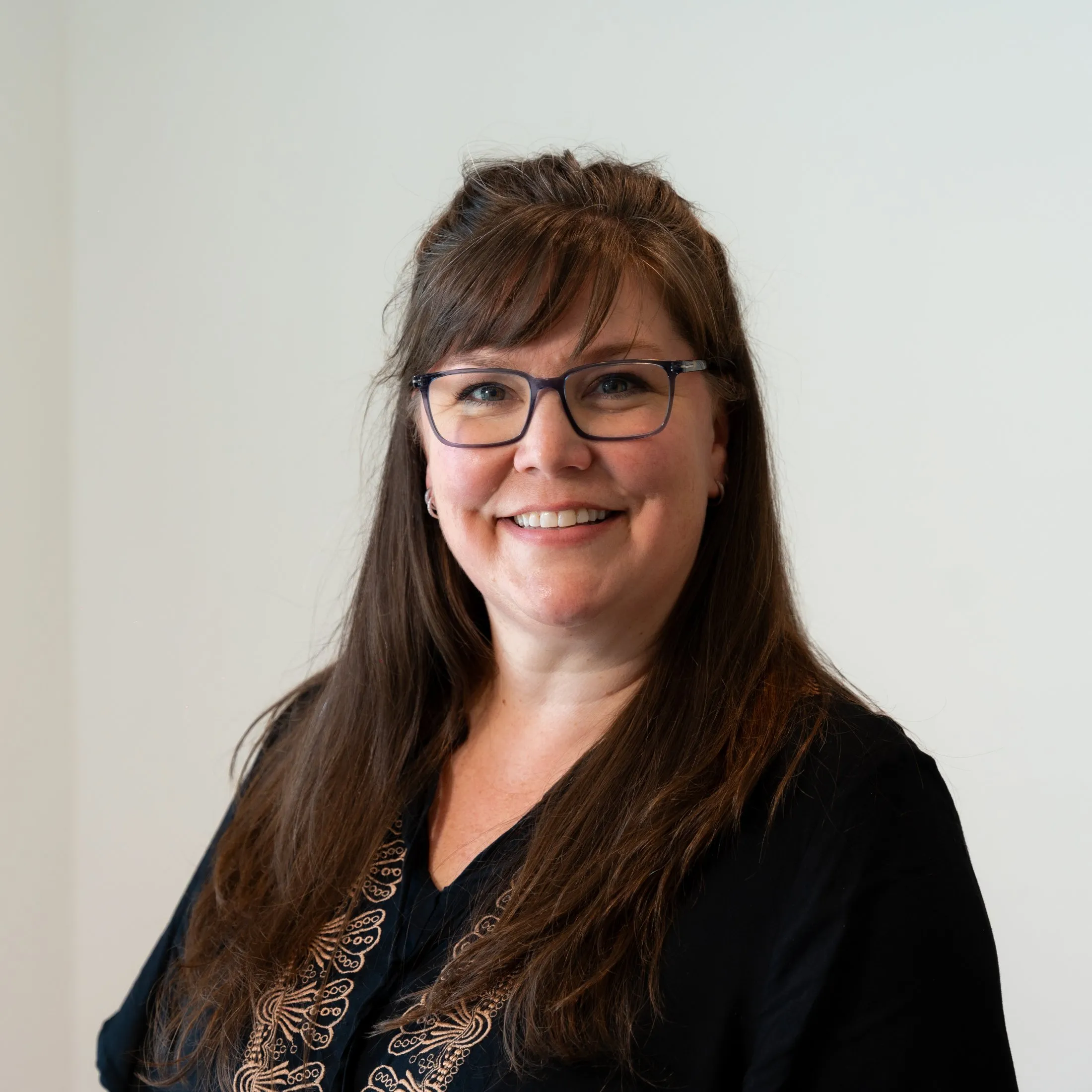 Smiling woman with glasses and long brown hair in black top