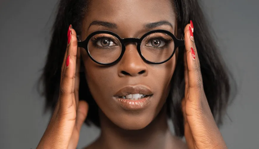 Woman with glasses and red nails touches temples, looking contemplative