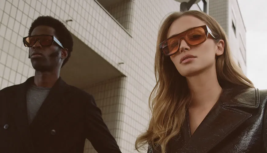 Two stylish people in leather jackets and sunglasses standing near urban building