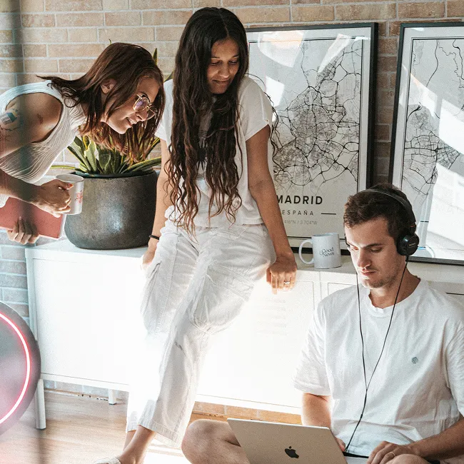 Three young people in casual white clothes collaborating in a bright room with city map posters and a laptop.