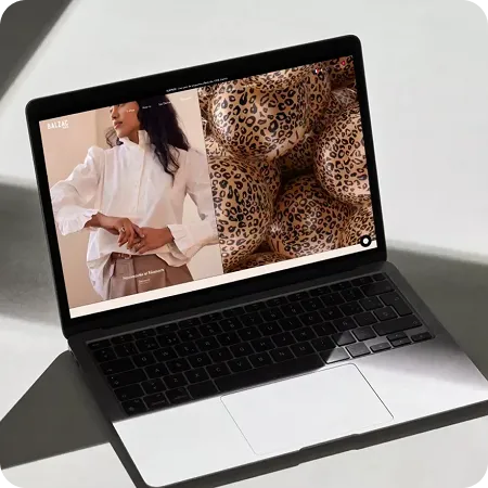 Open laptop displaying a fashion website with a woman in a white blouse and leopard-print balloons on the screen.