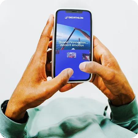 Person holding a smartphone displaying the Decathlon app with French text about innovation.