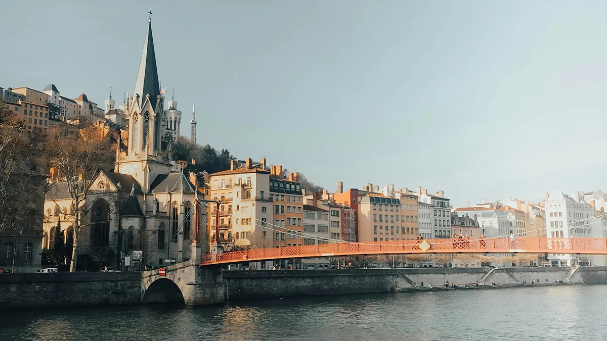 Cityscape with a historic church and a red bridge spanning a river under a clear sky.