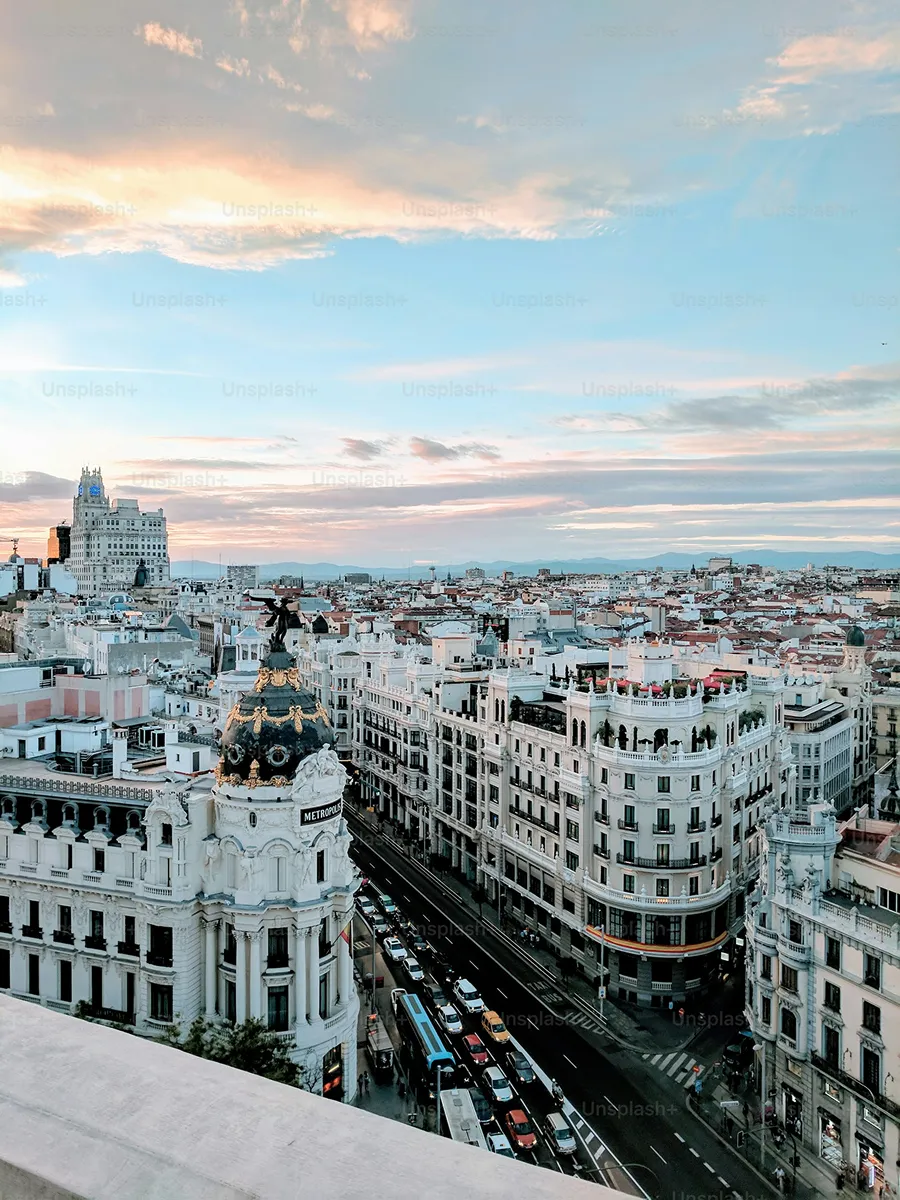 Aerial view of Madrid cityscape during sunset featuring the Metropolis Building with a black dome and gold accents, busy streets, and surrounding historic architecture.