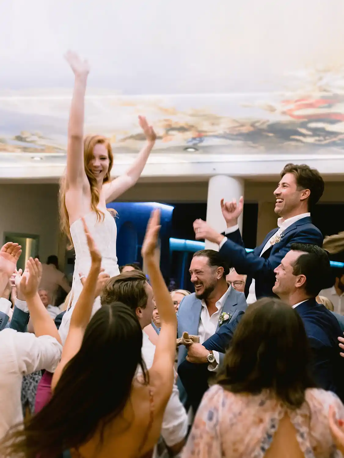 Bride lifted on guests shoulders under Bonj Beach Club Hvar fresco ceiling as crowd cheers on dance floor