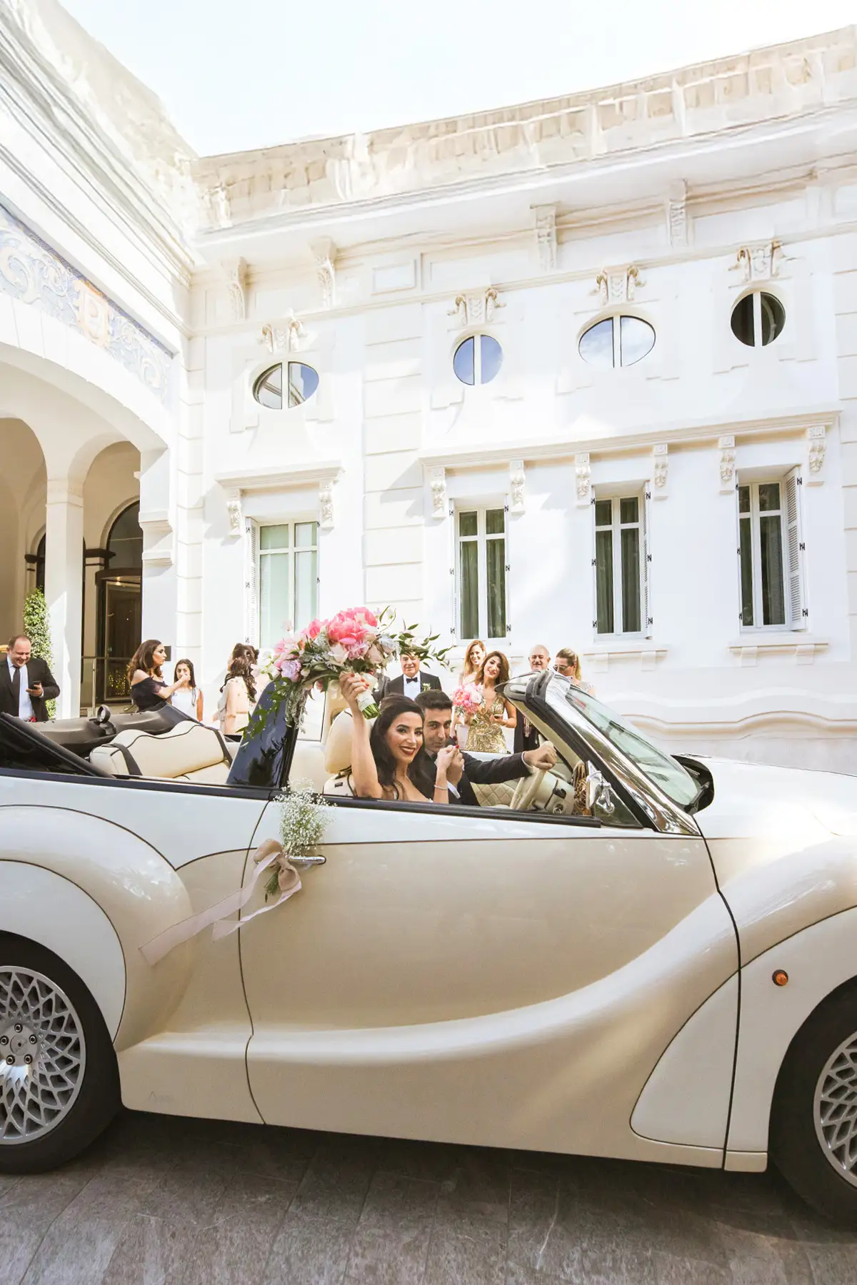 Couple in a cream vintage convertible outside Hotel Miramar, guests cheering and filming, Málaga
