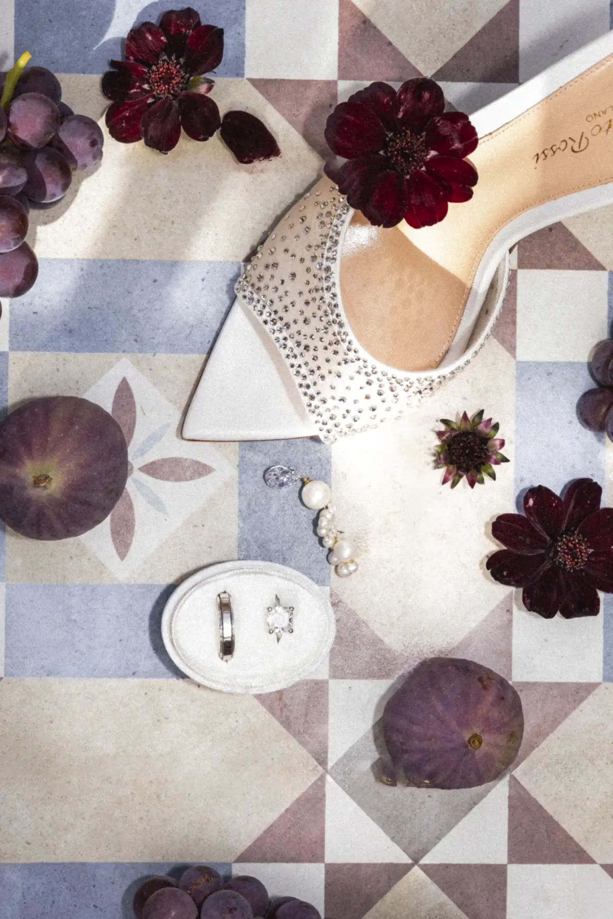 Crystal-embellished heel, dark red flowers, purple grapes and figs, a ring box, and a pearl earring