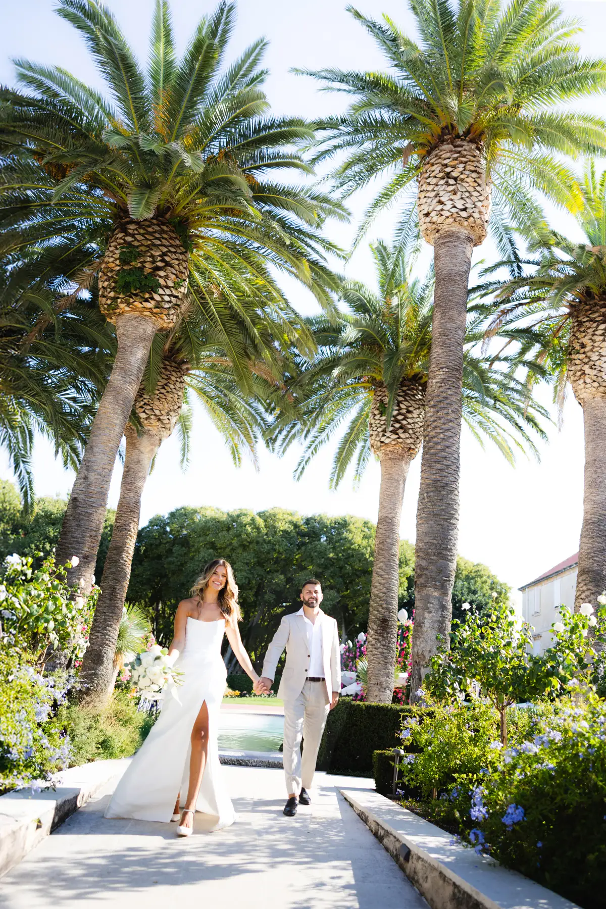 Couple walking a palm-lined garden path past clipped hedges and a reflecting pool, Hotel Lemongarden, Brač