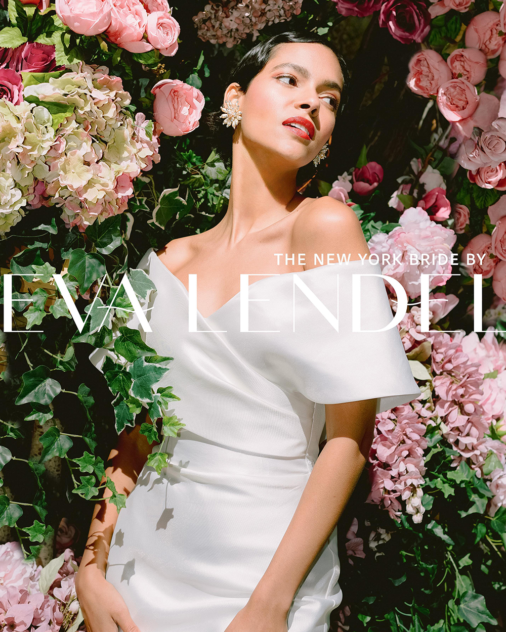 Bride in an off-shoulder Eva Lendel gown against a flower wall, Broadway, New York