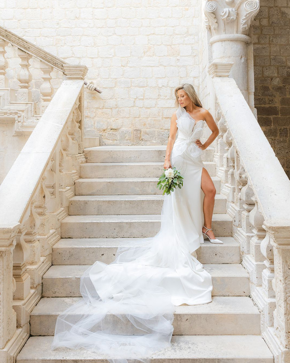 Bride on an ornate stone staircase with a carved balustrade, holding a bouquet, Rector's Palace, Dubrovnik