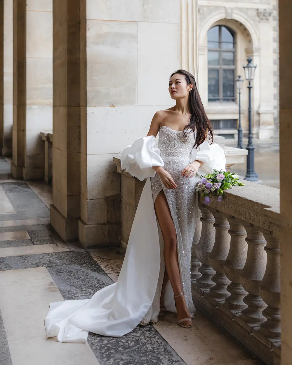 Bride in a sequined gown leaning against a stone balustrade in the Louvre's arcades, Paris