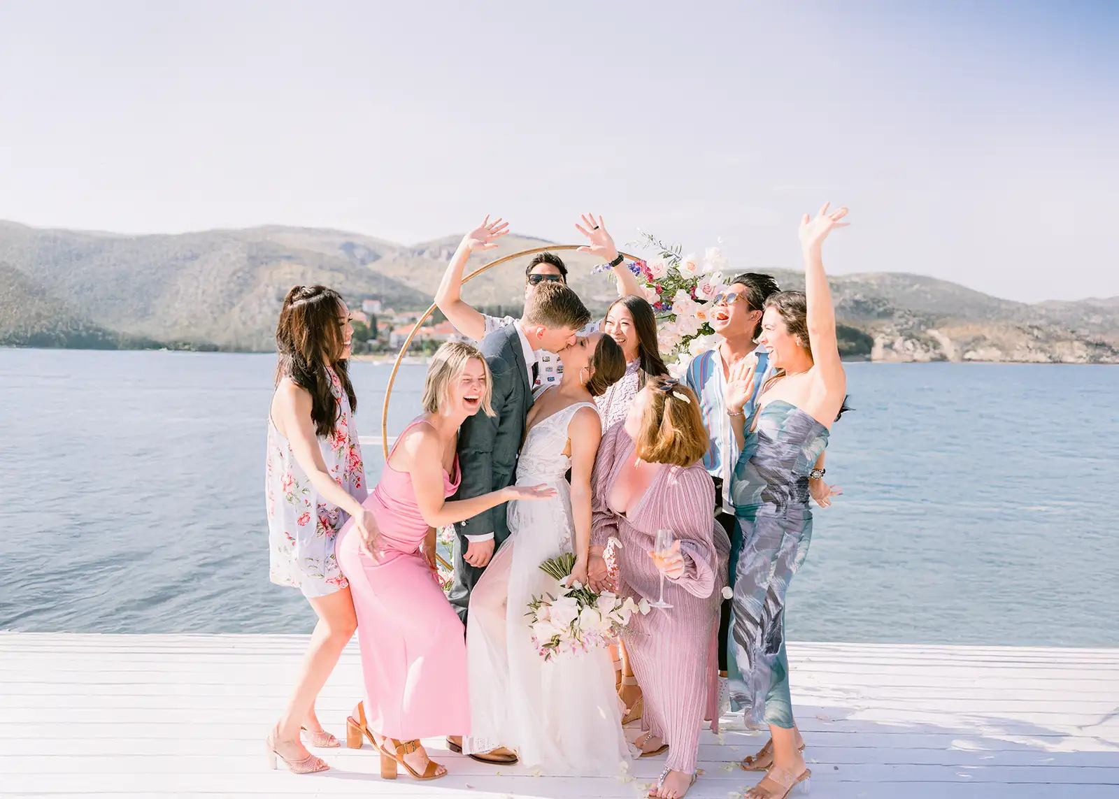 Guests crowd around a couple's kiss on a waterfront deck beneath a gold arch, Brown Beach House, Trogir.