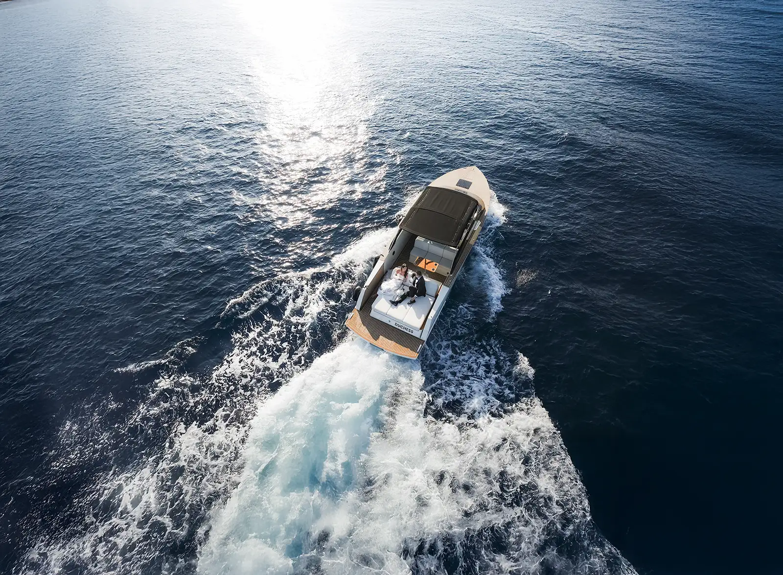 From above, a motor yacht cuts across open sea trailing a wide wake, a couple seated aft, Dubrovnik.