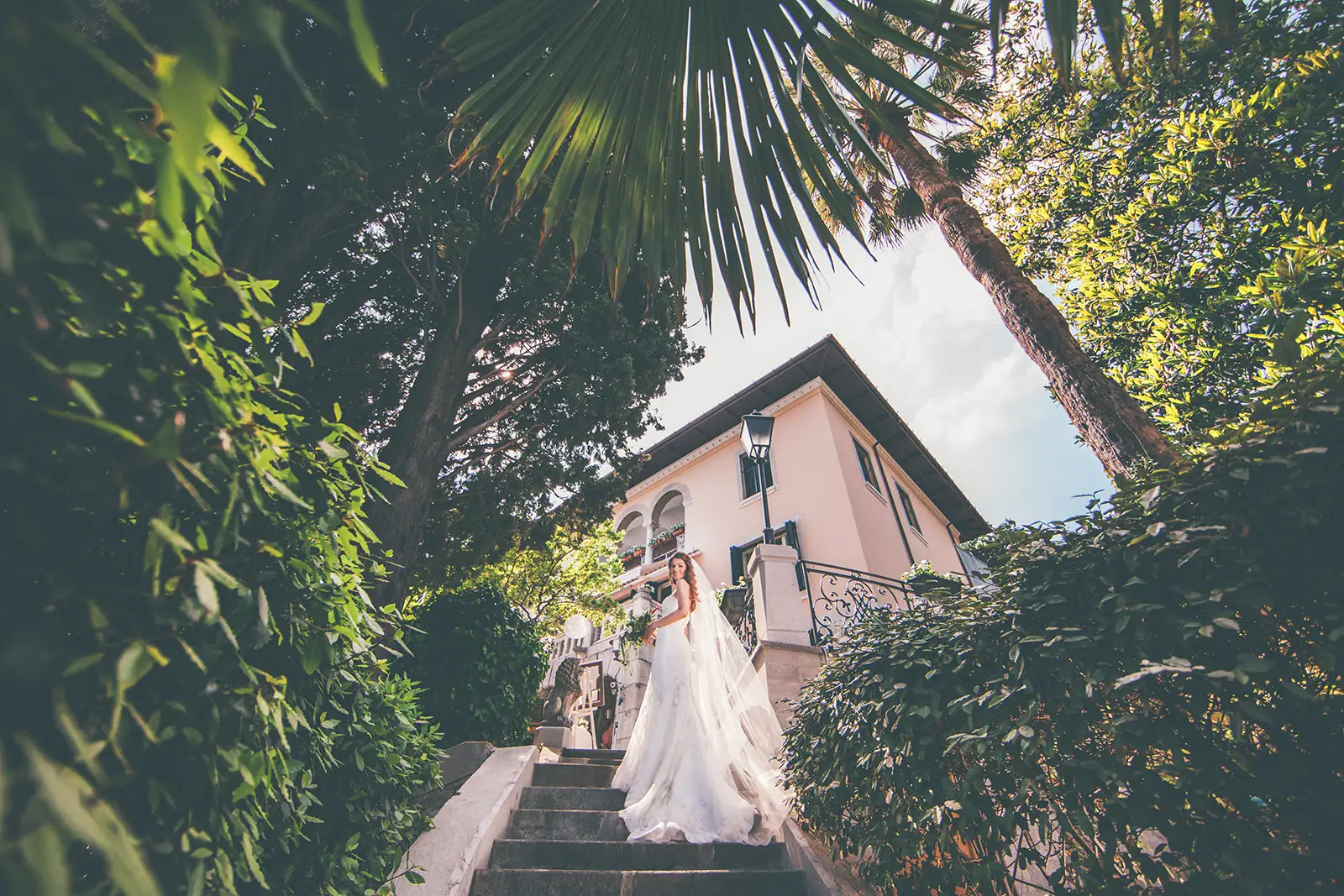 Bride in a lace gown and long cathedral veil on the garden stairs below Villa Ariston's pink facade, Opatija.