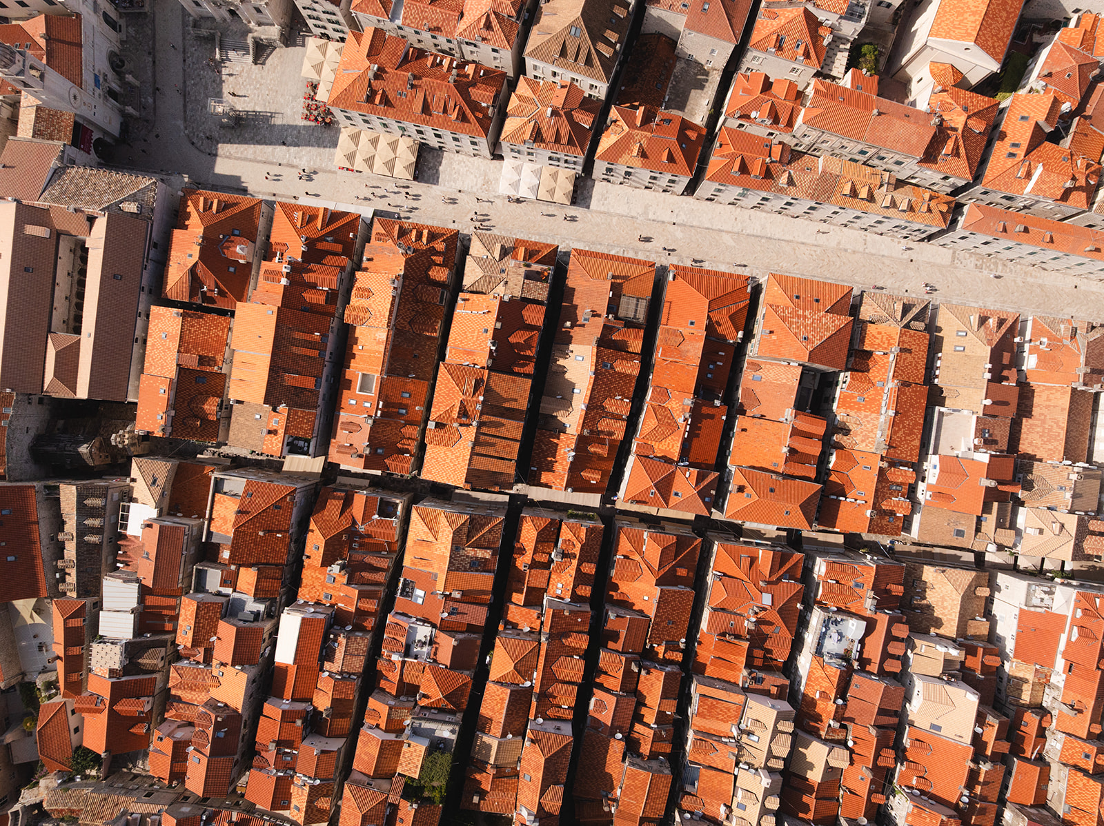 Aerial view looking straight down on rows of red-tiled rooftops and a stone pedestrian street