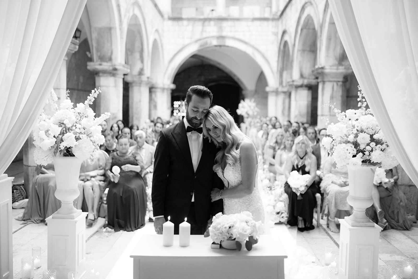 Bride and groom embrace at the altar during their ceremony as seated guests look on