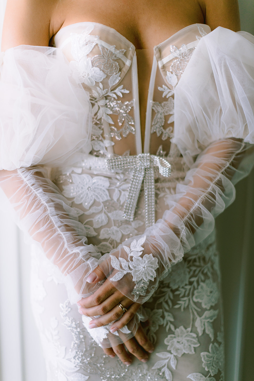 Close-up of a bride's lace wedding gown bodice and sheer lace gloves with clasped hands