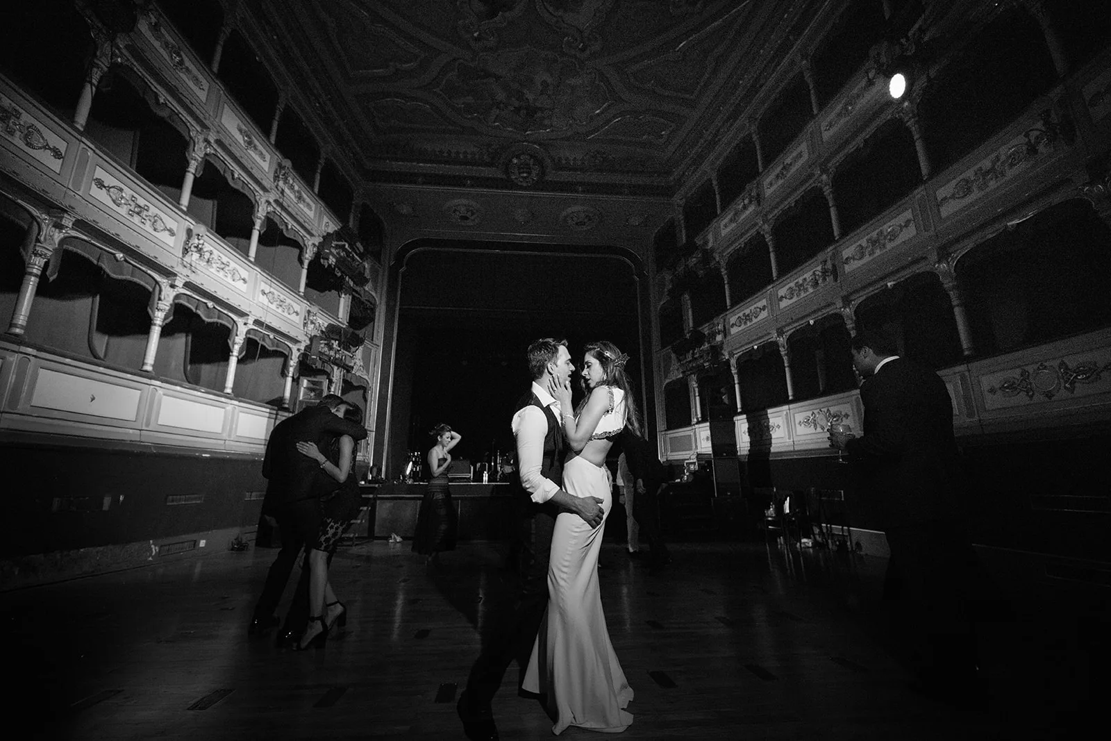 Bride and groom slow dance at the centre of a grand historic theatre, framed by tiers of gilded boxes.