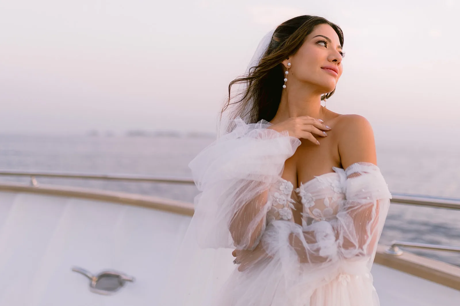 Close portrait of the bride on a yacht deck in golden-hour light, the hazy coastline behind her.