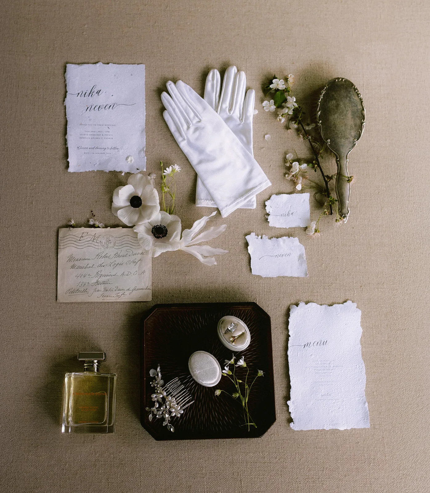 A styled flatlay of the couple's wedding stationery, vintage mirror, satin gloves and jewelry box, the calligraphed 'Nika, Neven' invitation naming the Zagreb venue.