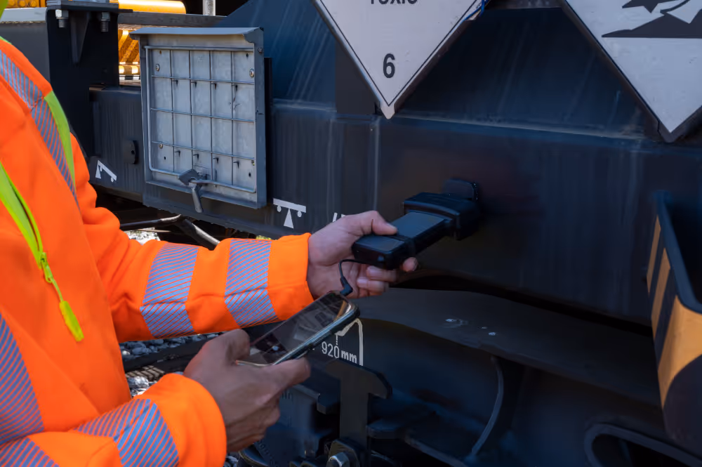Ein Bahnarbeiter bringt einen RFID Sensor an einem Eisenbahnwaggon an.
