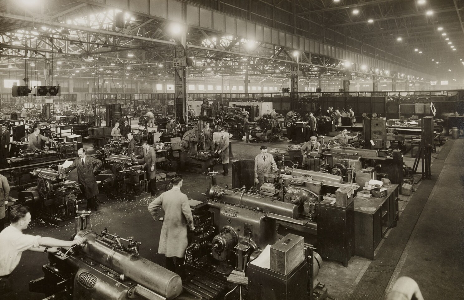Factory floor in the early 20th century showing workers operating machinery in a large, organised space, illustrating the application of Taylorism and scientific management principles.