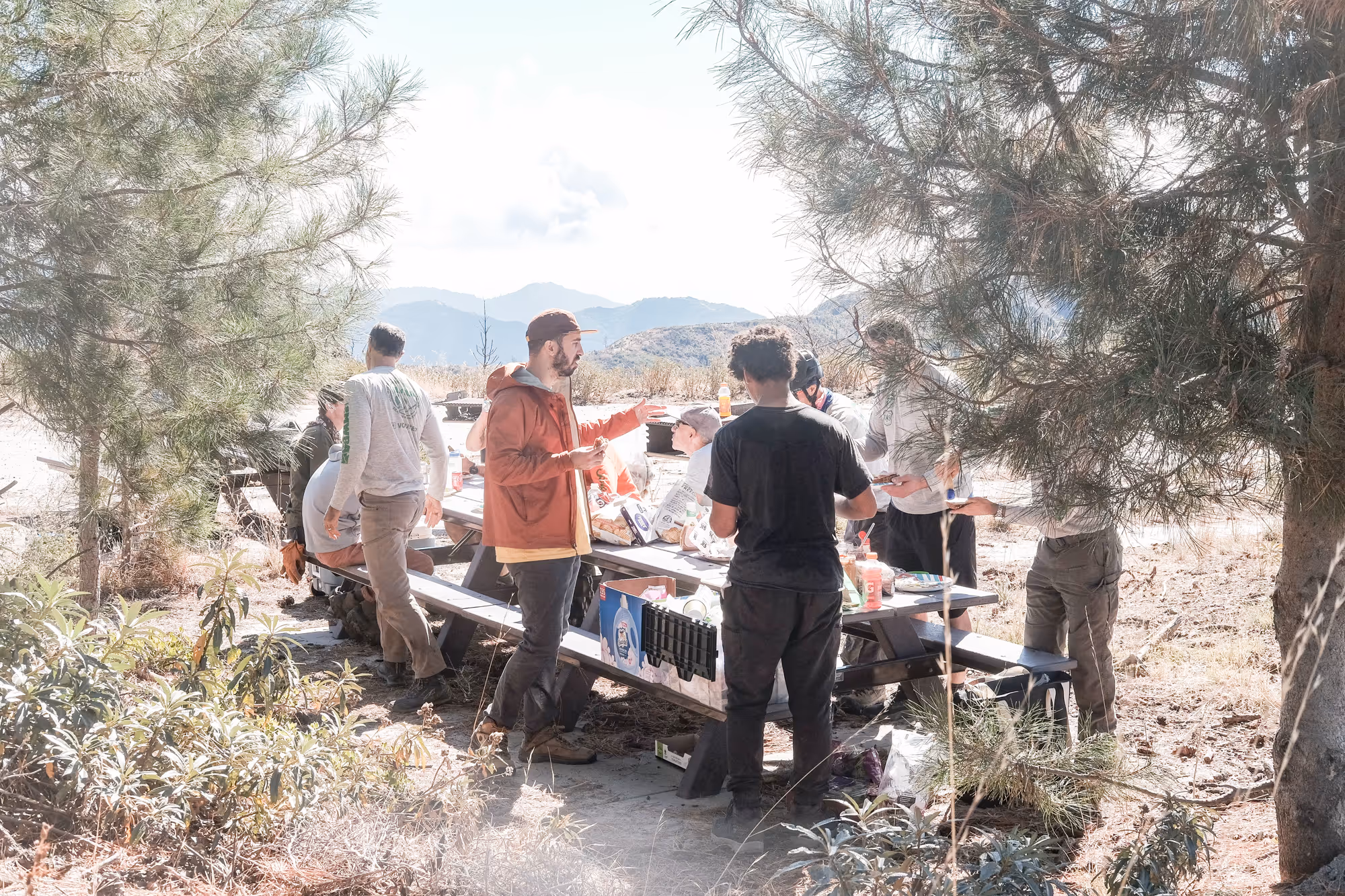 MWBA members grabbing food off an outdoor picnic table, with mountains in the background