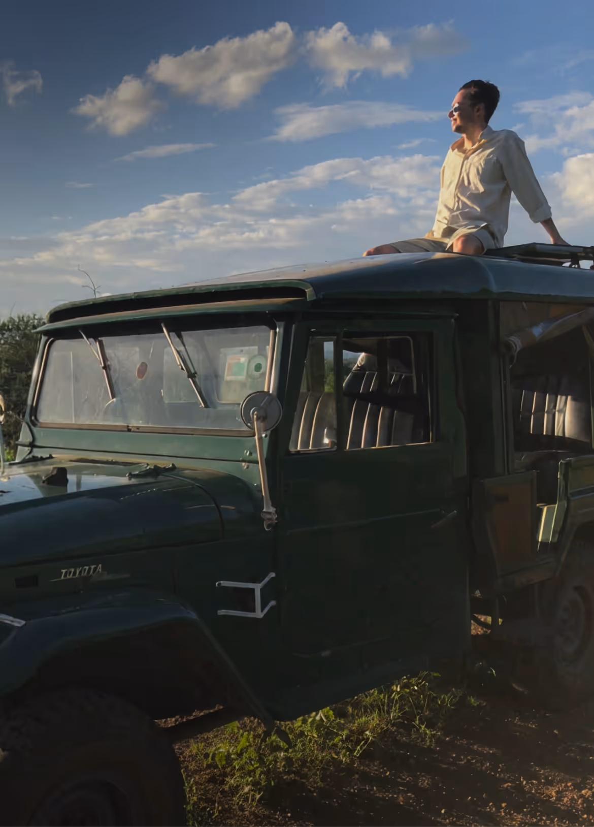 Mann sitzt auf dem Dach eines grünen Toyota-Geländewagens bei Sonnenuntergang.