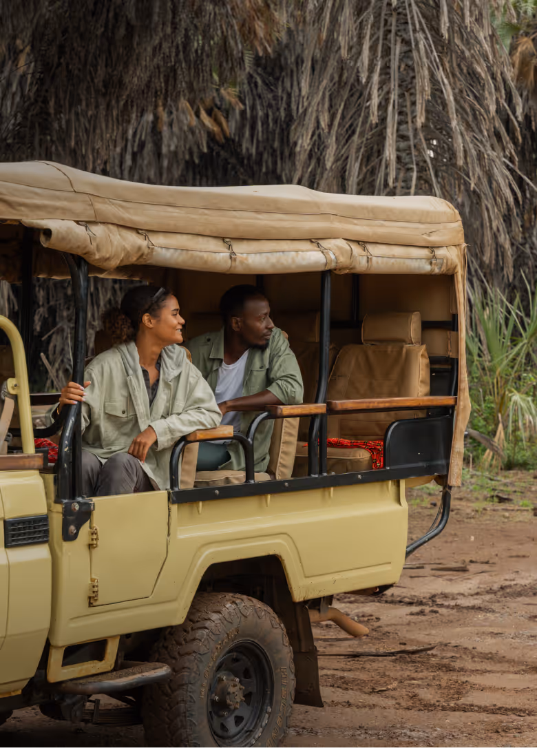 Zwei Menschen in Safari-Kleidung sitzen in einem offenen Safari-Geländewagen im Wald.