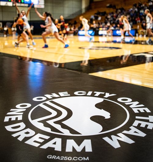 Gym floor logo with a bird and text 'One City One Team One Dream' during a girls basketball game.