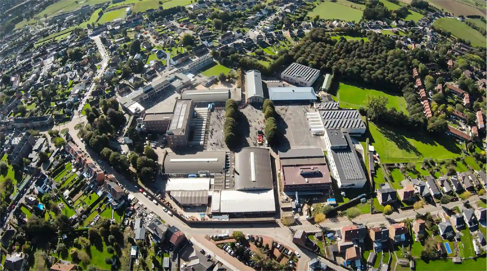 Luchtfoto van het schooldomein van Don Bosco Halle. Je ziet de gebouwen, de grote speelplaats, sportvelden en het bos.