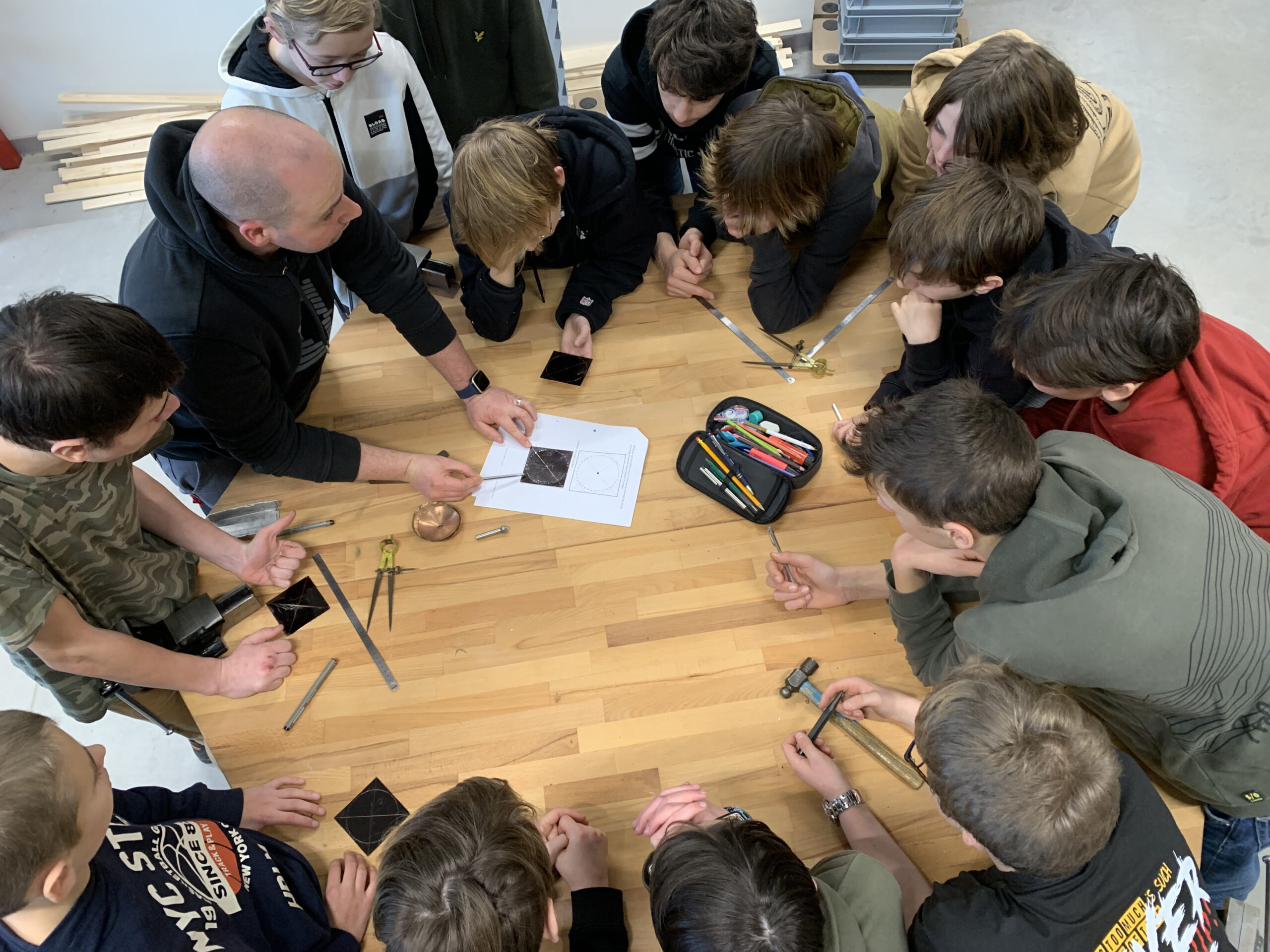 Leerkracht rond de tafel met een groep leerlingen. Leerkracht leg de leerlingen iets uit.