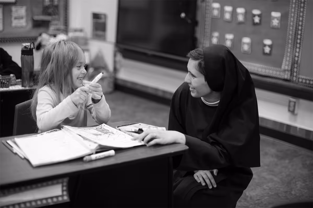 A sister kneeling beside a child at their desk and helping with school work